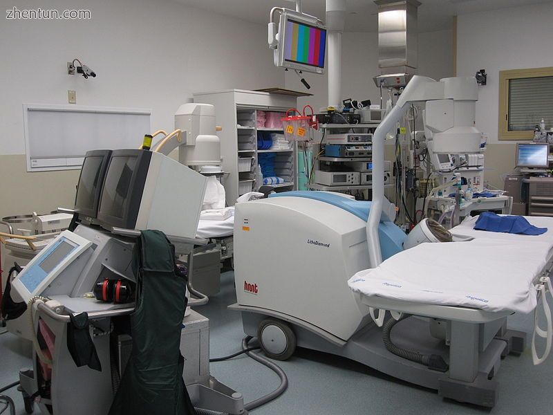A lithotriptor machine is seen in an operating room; other equipment is seen in the background, incl ...